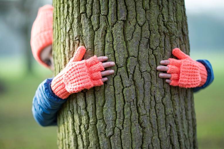 Person wearing gloves and hat hugging a mossy tree